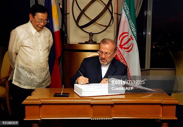 Philippine Foreign Secretary Alberto Romulo looks on as Iranian Foreign Minister Manouchehr Mottaki signs a guest book during a billateral meeting in...