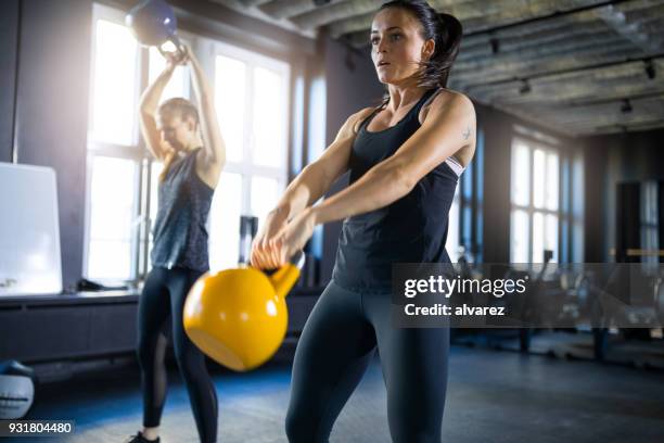 sportliche junge frauen schwingen kettlebells in turnhalle - kugelhantel stock-fotos und bilder