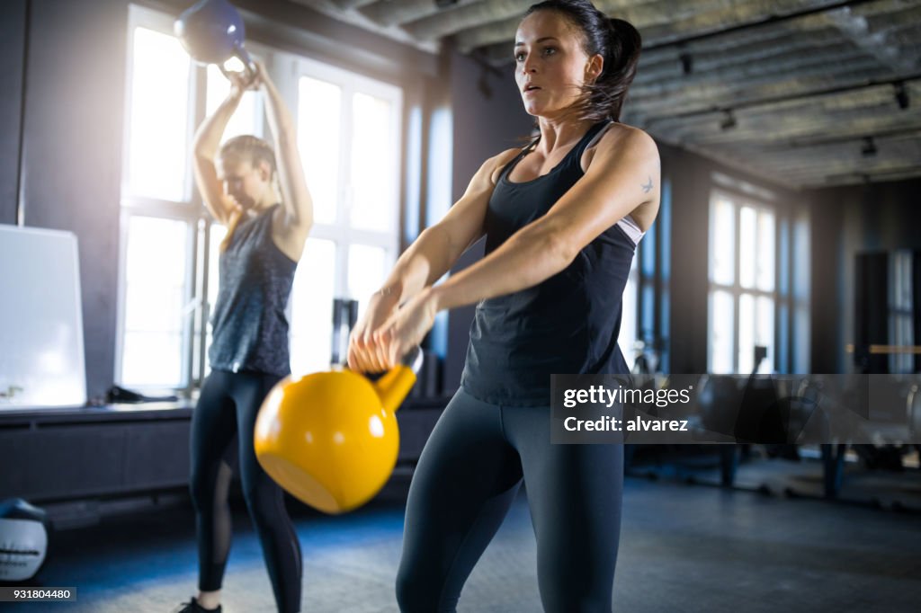 Mulheres jovens desportivos balançando kettlebells no ginásio