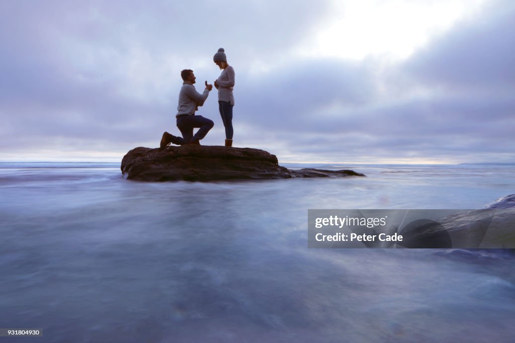 Man proposing to woman on rock in sea