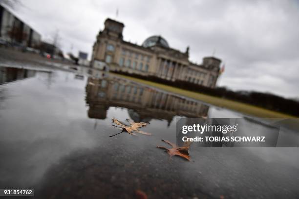 The Reichstag housing the Bundestag reflects in a puddle on March 14, 2018 in Berlin, as the new German government was sworn in here. German...