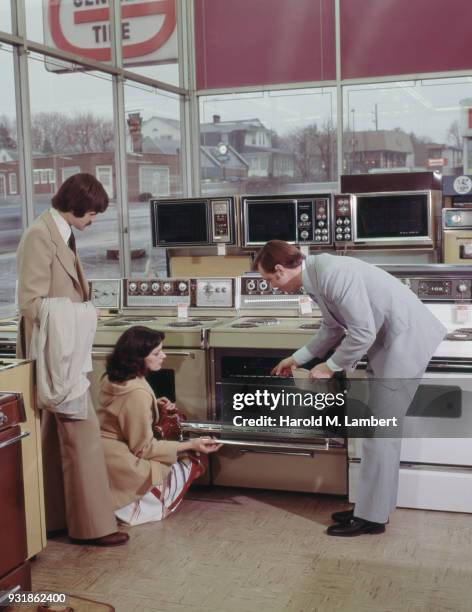 Store manager helping a couple who are looking for a new oven, 1977. Above them is a selection of Caloric microwave ovens.