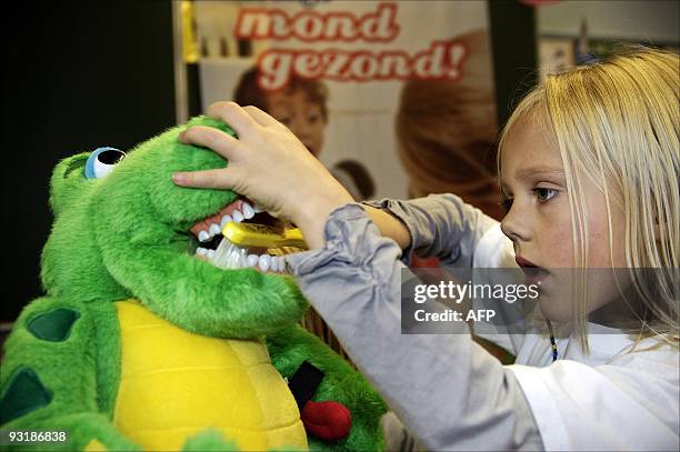 Child in a primary school practices brushing teeth on a green dragon stuffed animal as part of a project which teaches children how to properly brush...