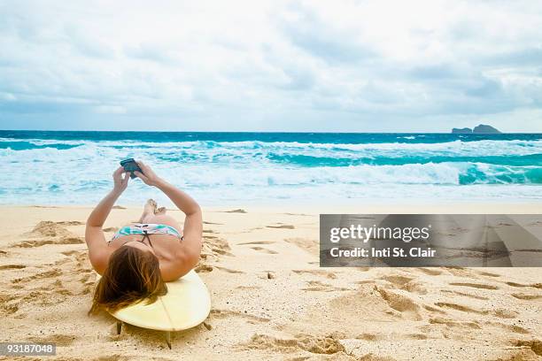woman laying on surfboard reading message on phone - funkwelle stock-fotos und bilder