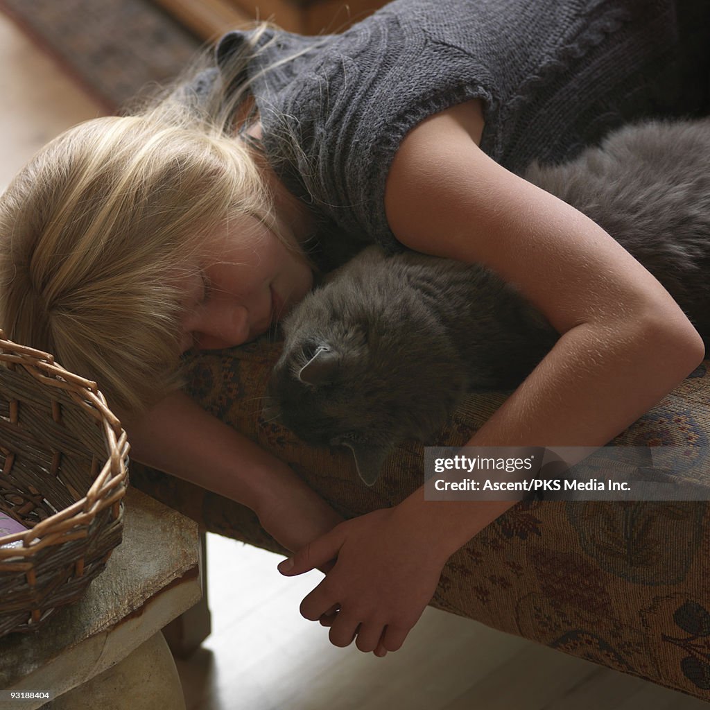 Girl cradles cat while sleeping on ottoman