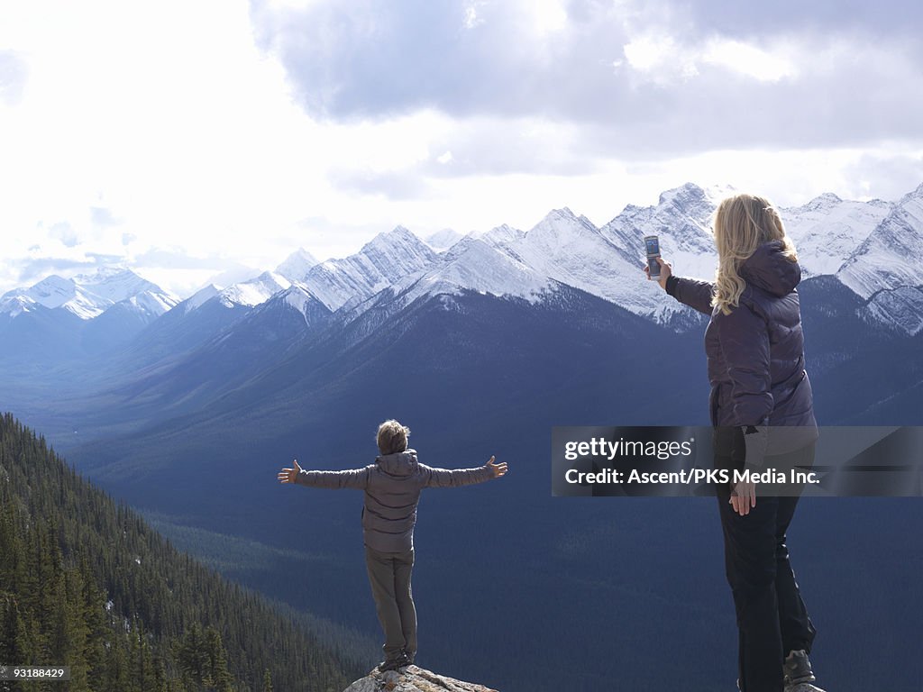 Woman takes picture of man on rock above valley