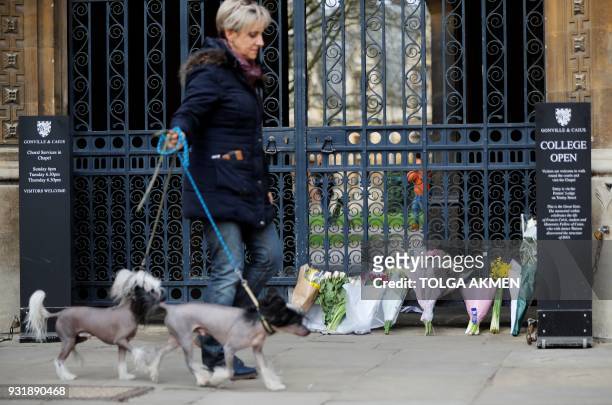 Woman walks her dogs past flowers left outside an entrance to Gonville and Caius College, where British physicist, Stephen Hawking was a fellow for...
