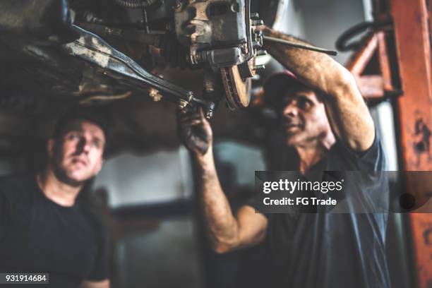 professional mechanic repairing a car in auto repair shop - mecânico imagens e fotografias de stock
