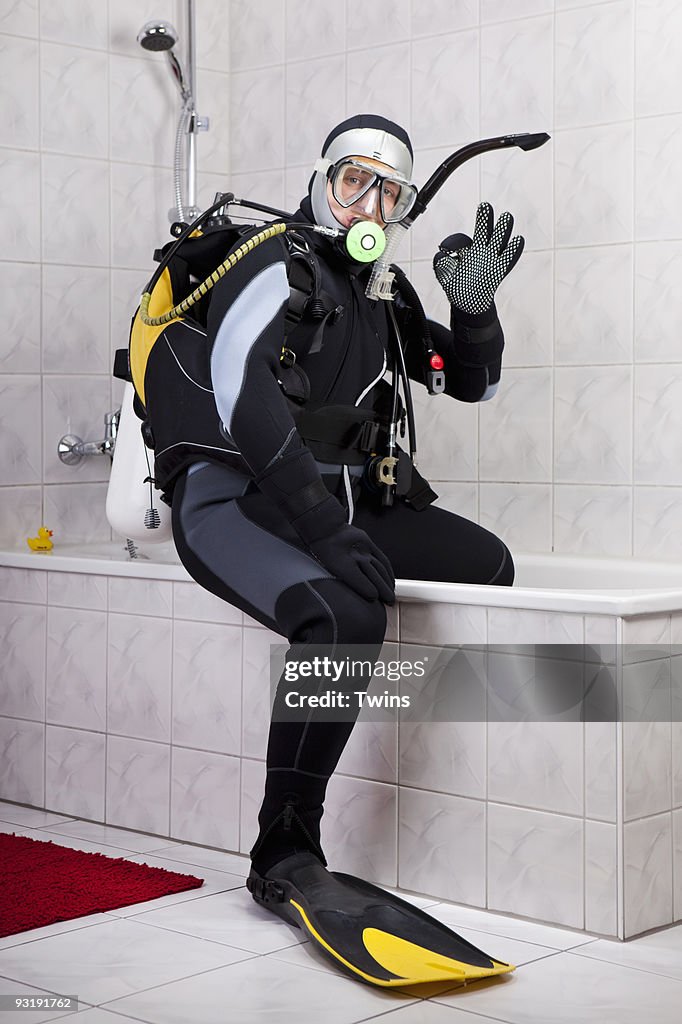 A scuba diver making the OK sign while sitting on the edge of a bathtub