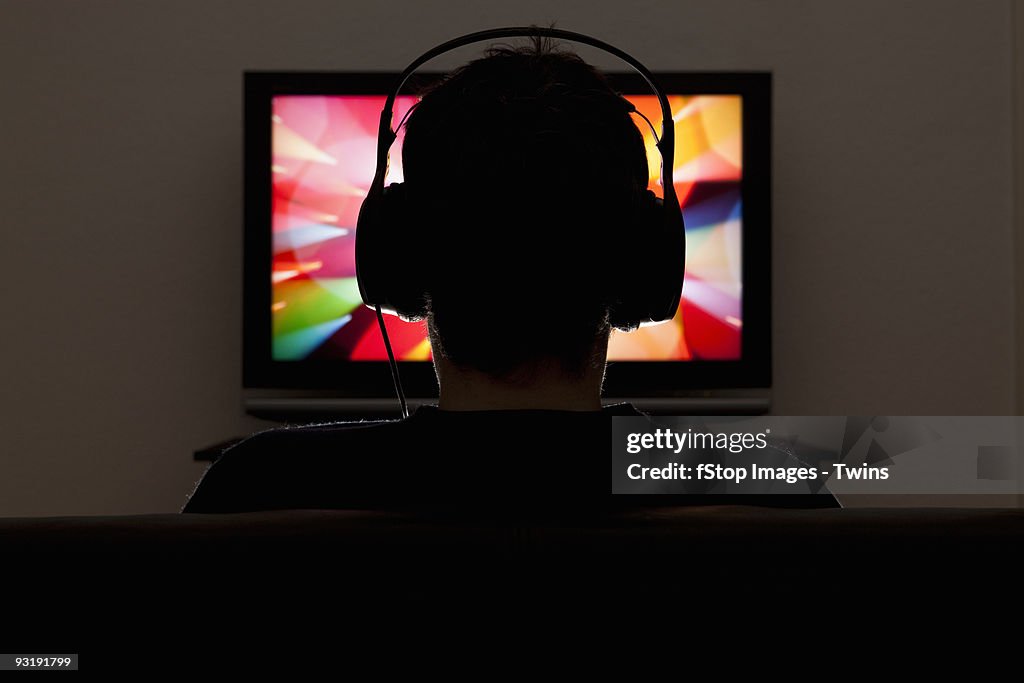 A man wearing headphones and watching television