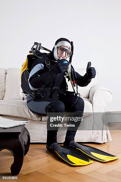 a scuba diver sitting on a couch in a living room giving a thumbs up sign - scuba mask stockfoto's en -beelden