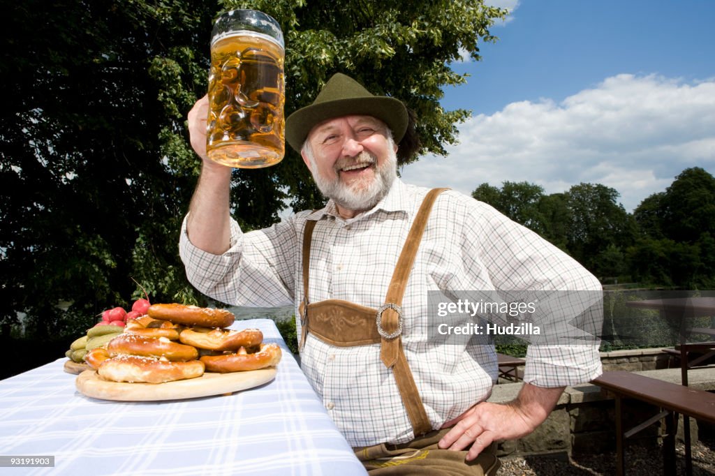 A traditionally clothed German man in a beer garden raising his beer glass in toast