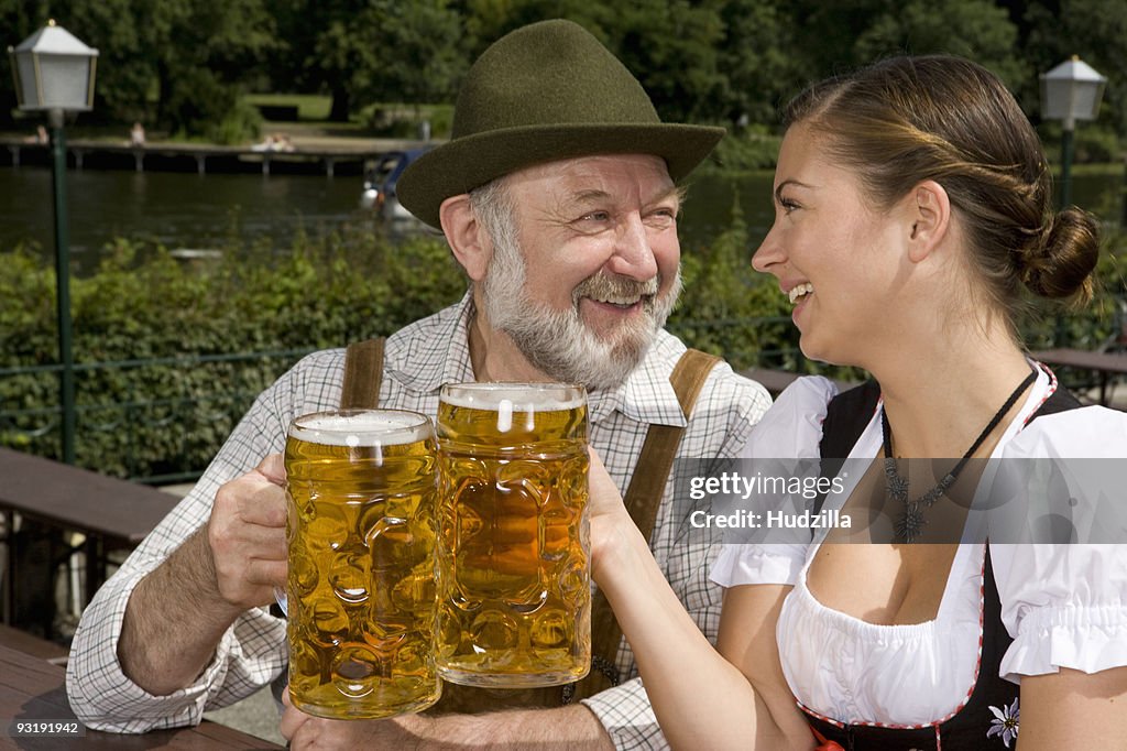 A traditionally clothed German man and woman in a beer garden toasting glasses