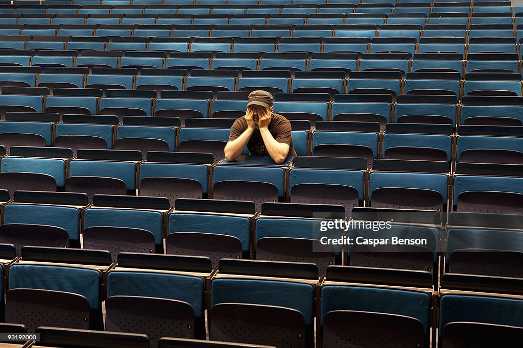 A man sitting in an auditorium, hands covering eyes