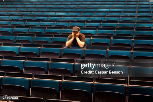 A man sitting in an auditorium, hands covering eyes A man sitting in an auditorium, hands covering eyes
