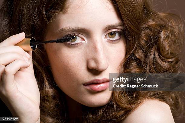 portrait of a young woman applying mascara - ojos marrones fotografías e imágenes de stock