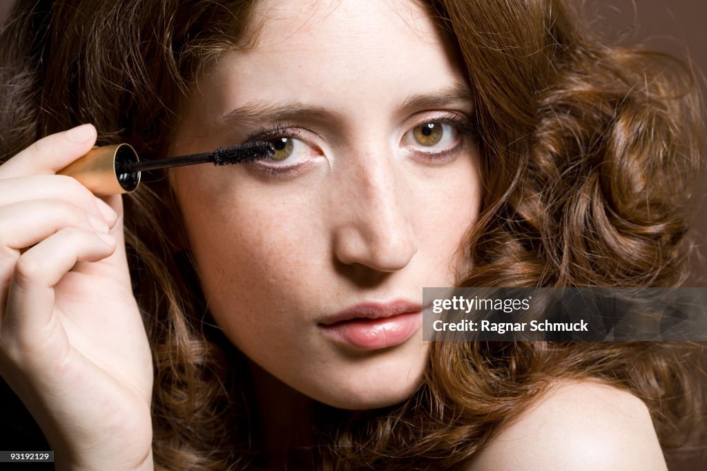 Portrait of a young woman applying mascara