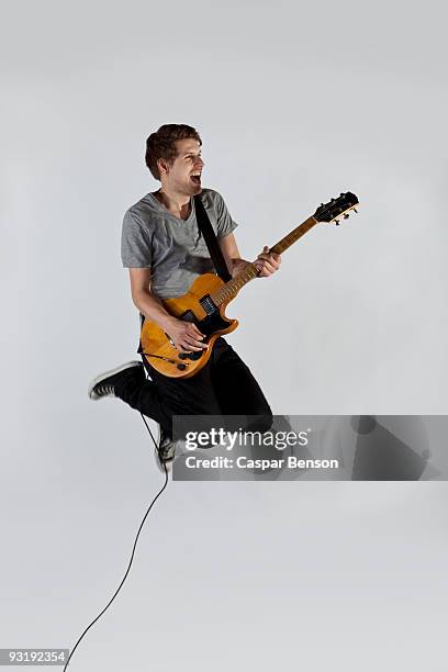 a musician playing a guitar and jumping in mid-air - electric guitar stock-fotos und bilder