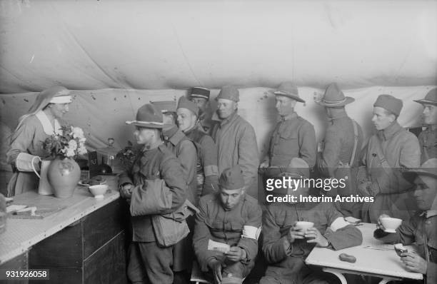 An American Red Cross canteen worker serves coffee, doughnuts, and sandwiches to a line of soldiers, Toul, France, June 22, 1918. In the foreground,...