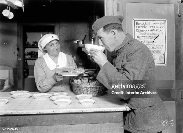 An American Red Cross canteen worker offers a plate of bread to a soldier as he drinks a cup of coffee, Chateauroux, France, October 31, 1918.