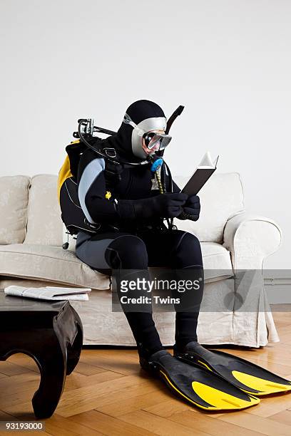 a scuba diver sitting on a couch reading a book - buceo con equipo fotografías e imágenes de stock