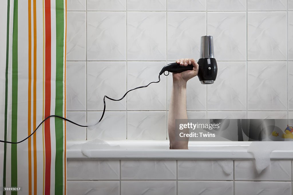 A human hand sticking out of a bathtub holding a hairdryer