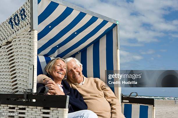 a senior couple sitting together in a hooded beach chair - beach shelter ストックフォトと画像