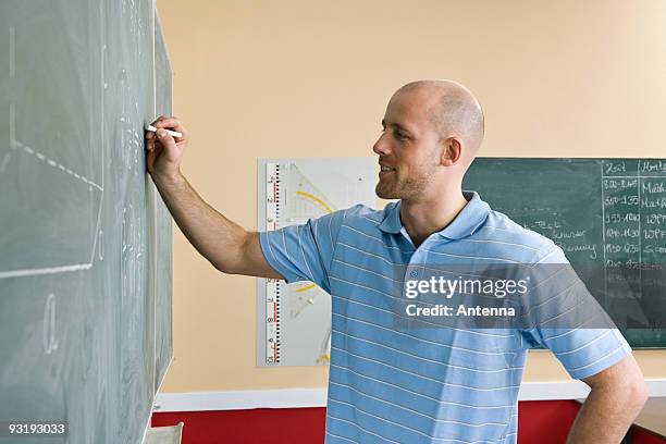 a male teacher writing on a blackboard - male teacher in a classroom stock-fotos und bilder