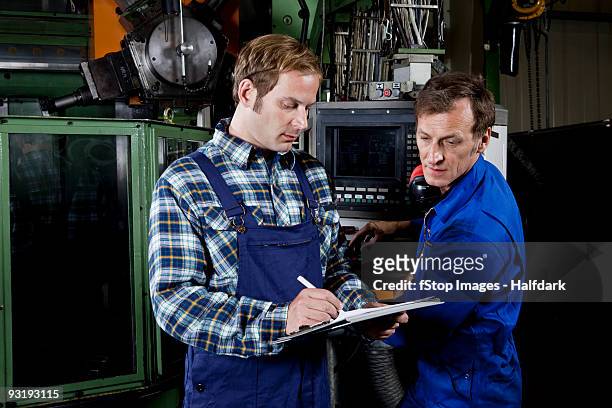 two men in a metal parts factory reviewing a clipboard - réfléchir écrire adulte 40 ans papiers photos et images de collection