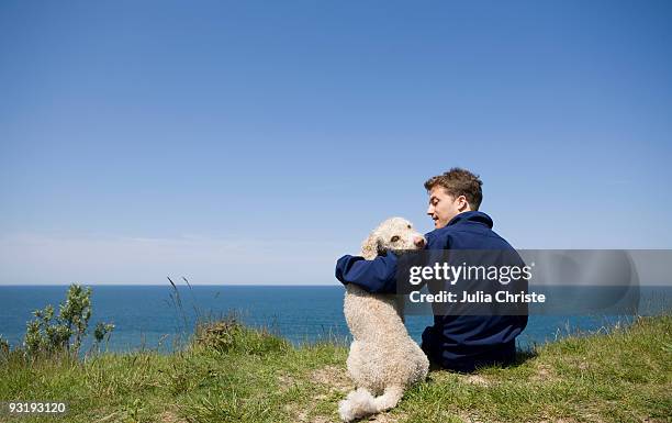 a man with his arm around a dog sitting by the sea - hairy back man stock pictures, royalty-free photos & images
