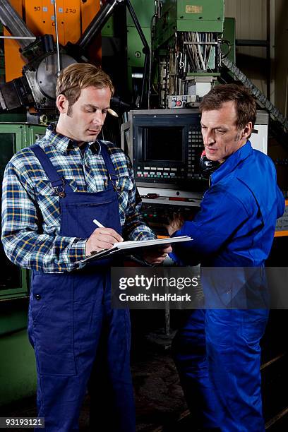 two men in a metal parts factory reviewing a clipboard - réfléchir écrire adulte 40 ans papiers photos et images de collection