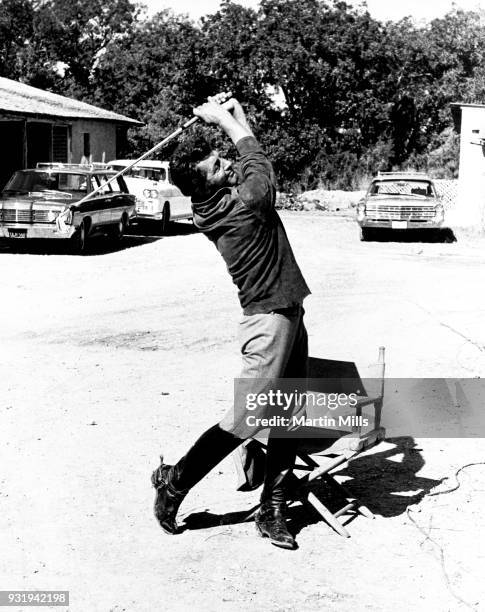 Entertainer Dean Martin swings a golf club while sitting on the set of the 20th Century Fox film 'Bandolero!' in 1967.