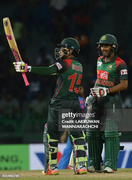 Bangladesh cricketer Mustafizur Rahman is watched by his teammate Sabbir Rahman as he raises his bat to the crowd after scoring a half-century during...