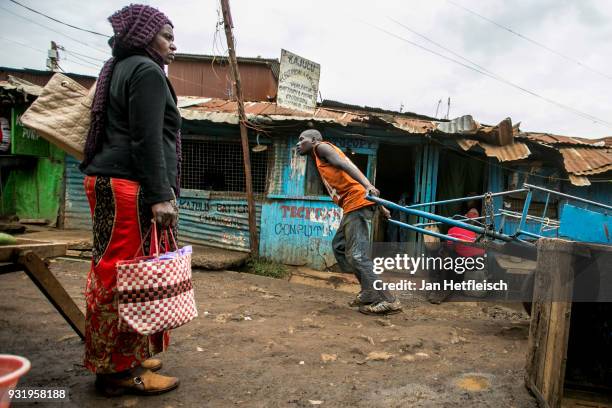 Man pulls a handbarrow through the muddy streets of the Kibera slum on March 12, 2018 in Nairobi. Kibera is located 6KM south west of the city centre...