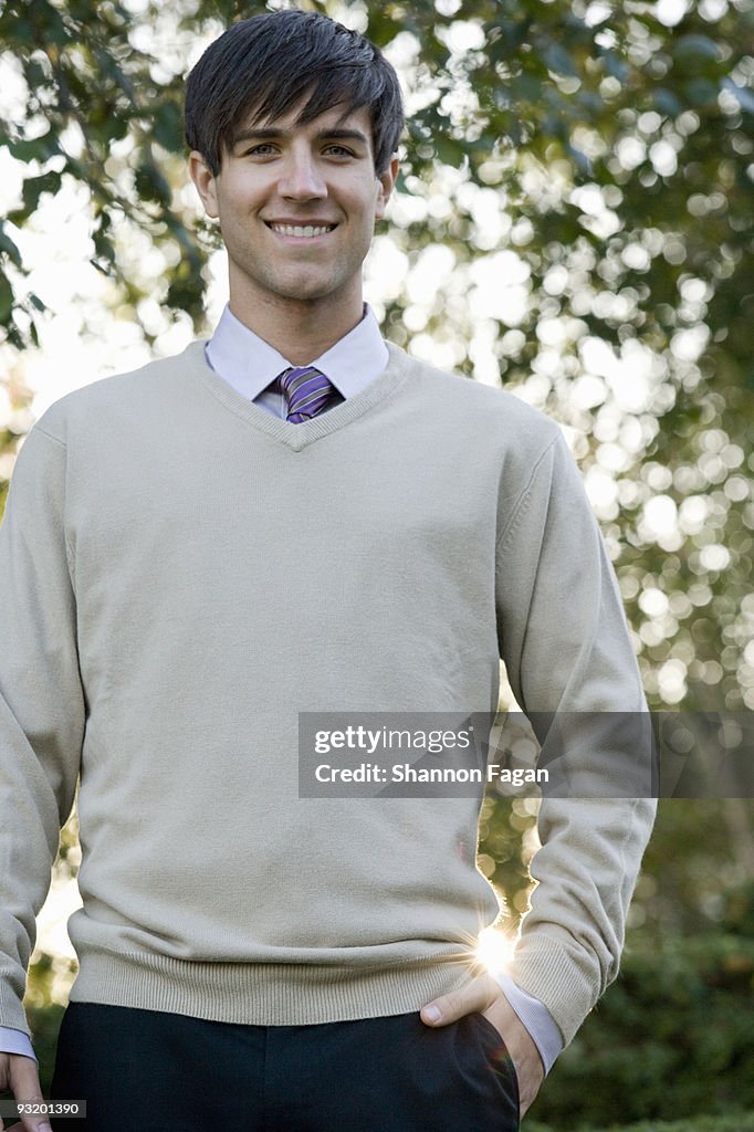 Man in suit smiling with hand in pocket at garden