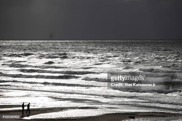 two men on beach, rough sea - katsouras stock-fotos und bilder