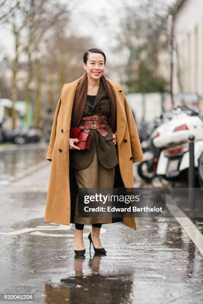 Guest wears a long camel coat, a brown scarf, a red clutch, a khaki jacket, a yellow bronze long skirt, black leggings, black stilettos, a red double...