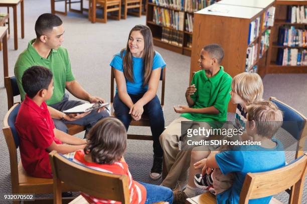 giovane insegnante conduce dopo scuola club in biblioteca - bambini seduti in cerchio foto e immagini stock