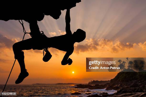 silhouette of rock climber climbing an overhanging cliff with sunset - rock overhang foto e immagini stock