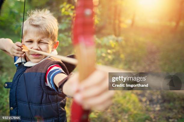 kleiner junge schießen bogen im wald - bogenschießen stock-fotos und bilder