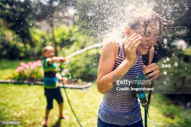 enfants ayant des éclaboussures fun dans back yard - water sprayer photos et images de collection