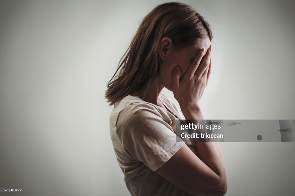 Portrait of depressed woman, covering face with her hands, side view