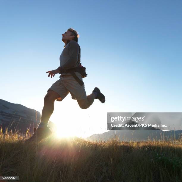 man runs on grass hillside, above rising sun - running in the sun stock-fotos und bilder