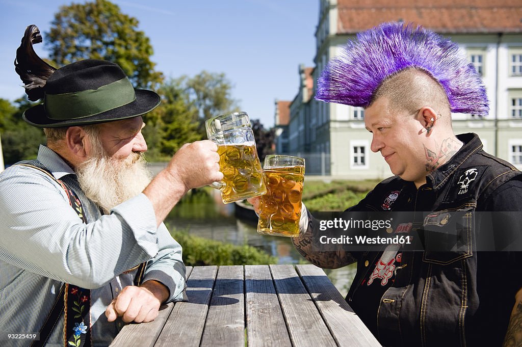Germany, Bavaria, Upper Bavaria, Man with mohawk hairstyle and Bavarian man holding beer stein glasses