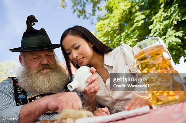 germany, bavaria, upper bavaria, bavarian man and asian woman in beer garden, bavarian man sniffing snuff - snuff bottles foto e immagini stock
