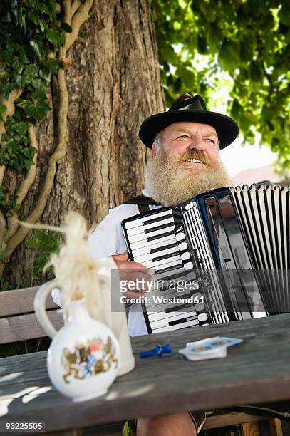 germany, bavaria, upper bavaria, senior man in traditional costume playing accordion in beer garden - snuff bottles foto e immagini stock