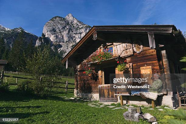 austria, karwendel, senior man sitting in front of log cabin, reading a book - holiday house stock pictures, royalty-free photos & images