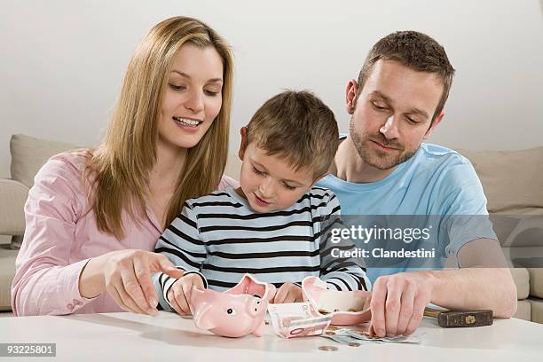 parents and son (4-5) looking at broken piggybank, counting money - eltern geld stock-fotos und bilder