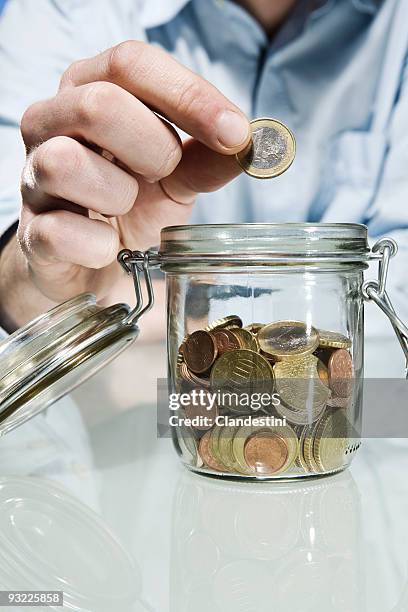 person putting euro coin into preserving jar, close up - moneta da un euro foto e immagini stock
