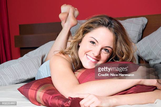 young woman lying on bed, smiling, portrait - woman lying on stomach with feet up stock pictures, royalty-free photos & images